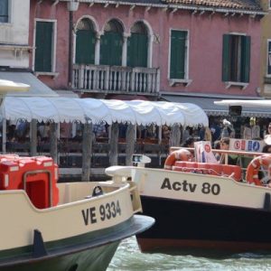ACTV Vaporetto waterbuses in the middle of a Venetian canal; there are people on them