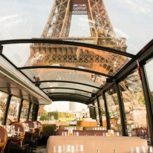 tables, glasses, silverware inside the Bustronome bus; glass ceiling; view of the lower part of the Eiffel Tower