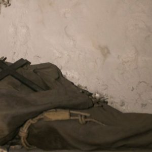 a corpse dressed in a monk's robe and hood; it's carrying a cross