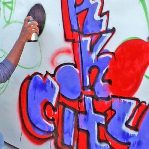 girl wearing an orange beanie using black spray paint on a wall canvas
